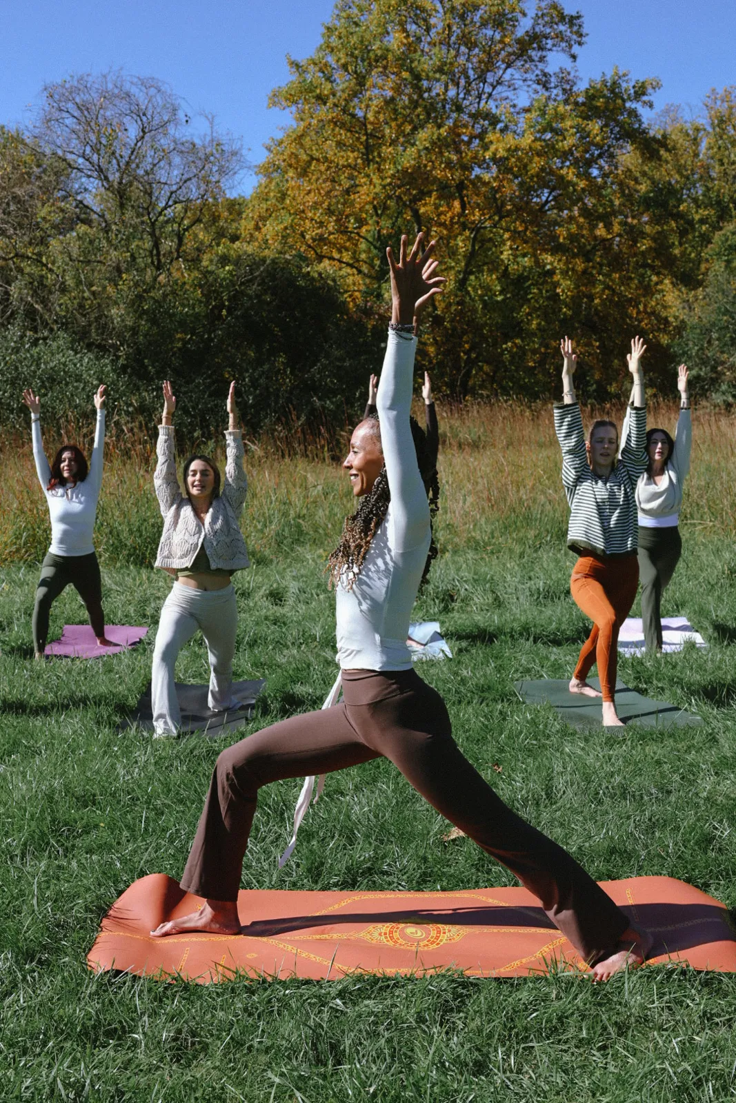Group in warrior pose on mats in an autumn field