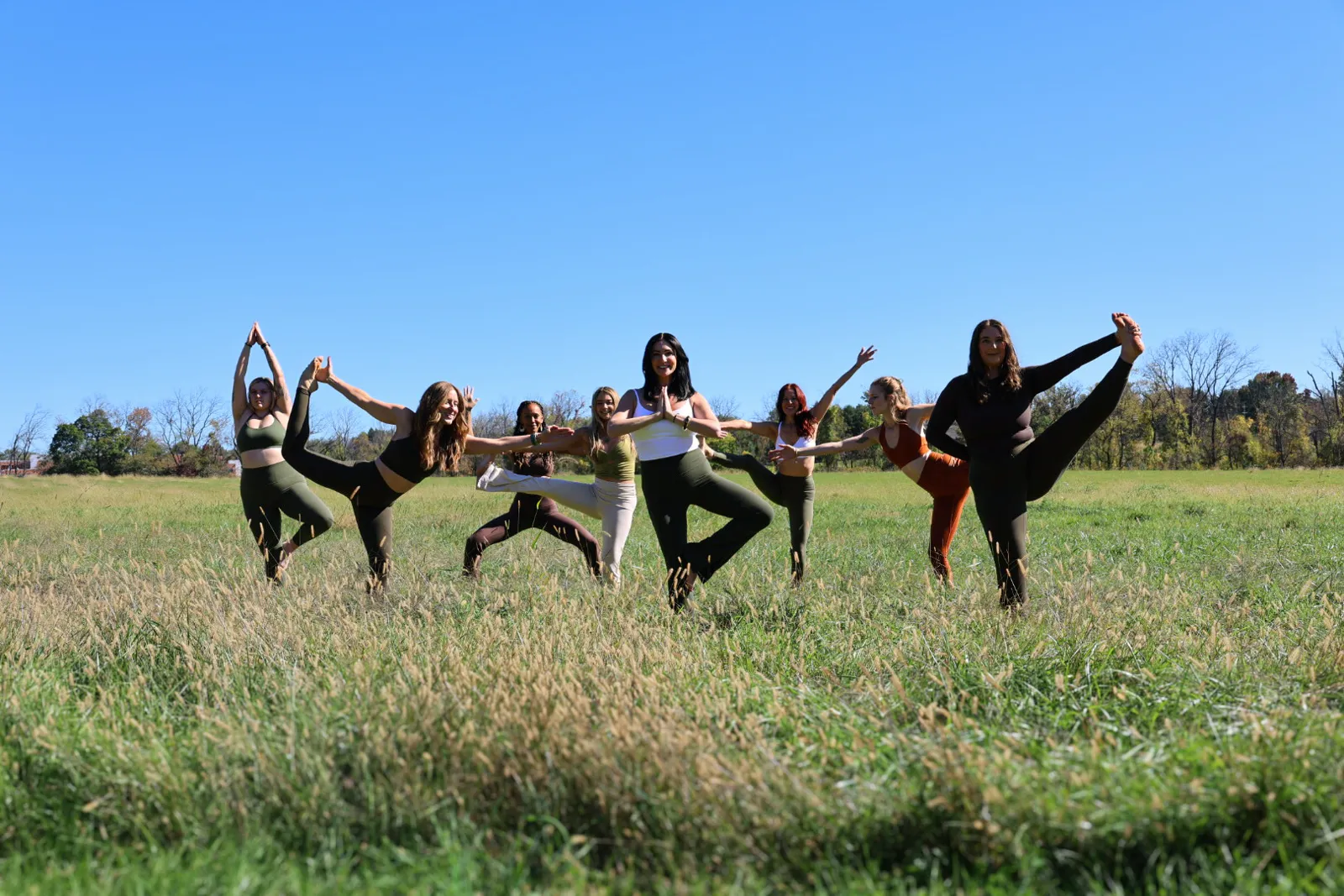 Group balancing together in dancer pose across an open meadow